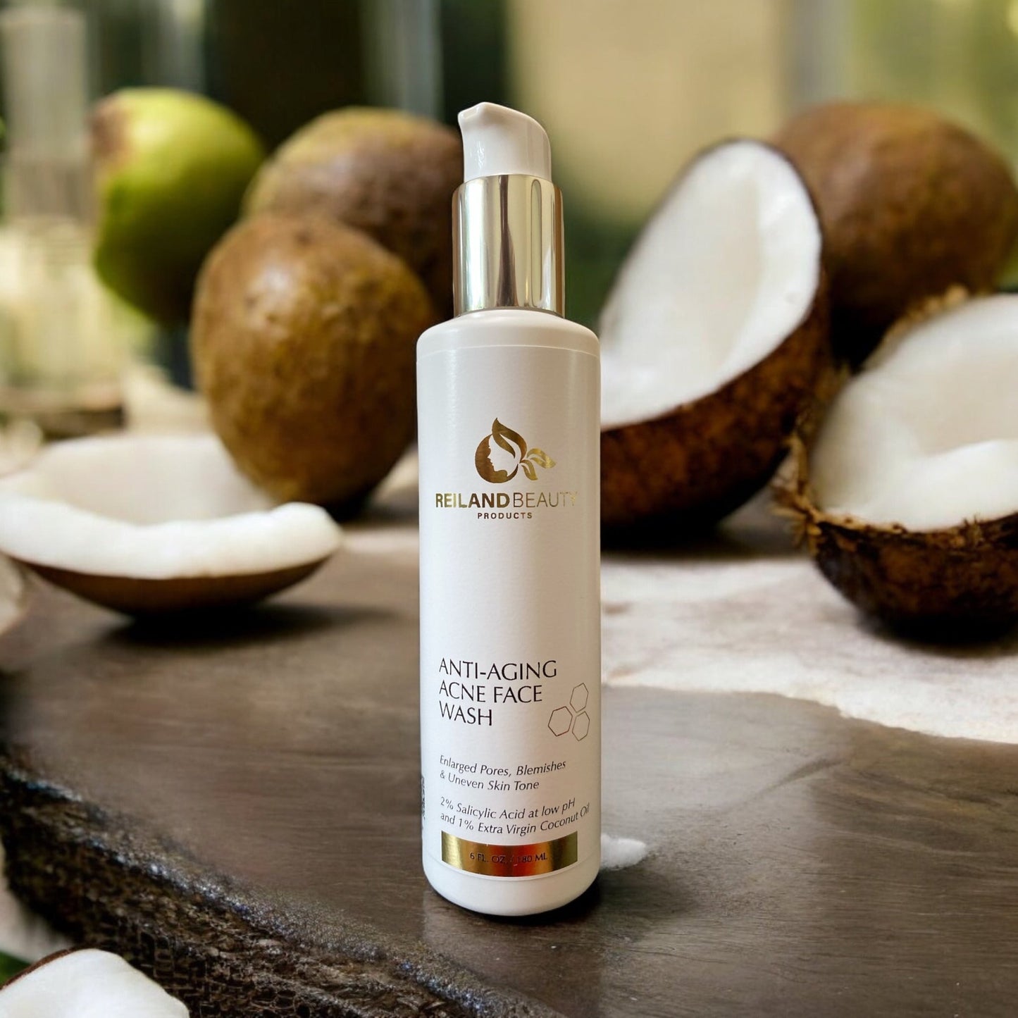 Reiland Beauty Products Anti-Aging Acne Face Wash bottle displayed on a natural surface with open coconuts in the background. Features 2% salicylic acid and 1% extra virgin coconut oil for blemish control and gentle exfoliation.