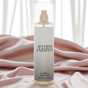 High-quality image of the Jennifer Aniston Fine Fragrance Mist (8 oz / 236 ml) displayed upright on soft pink satin fabric with sheer white curtains in the background. The image evokes a luxurious, feminine, and elegant atmosphere — ideal for promoting premium scent experiences. Perfect for use on Shopify, TikTok Shop, and beauty campaigns.