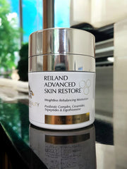 Elegant image of Reiland Advanced Skin Restore on a glossy surface with natural lighting, highlighting the product’s luxurious silver finish and active ingredients.