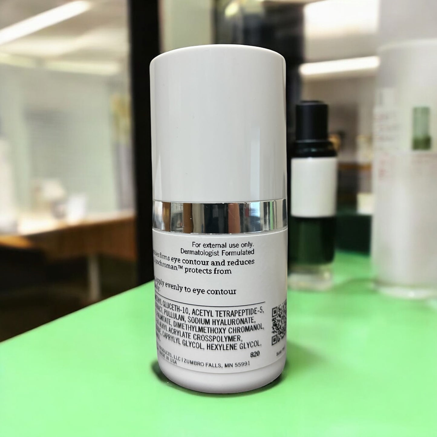 Rear label of Reiland Ultra Benefit Eye Gel in a spa-clinic setting with other skincare bottles in view, conveying a professional skincare environment.
