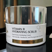 High-resolution close-up of Reiland Vitamin B Hydrating Scrub jar placed on a glossy surface with ambient light reflecting from the silver lid.
