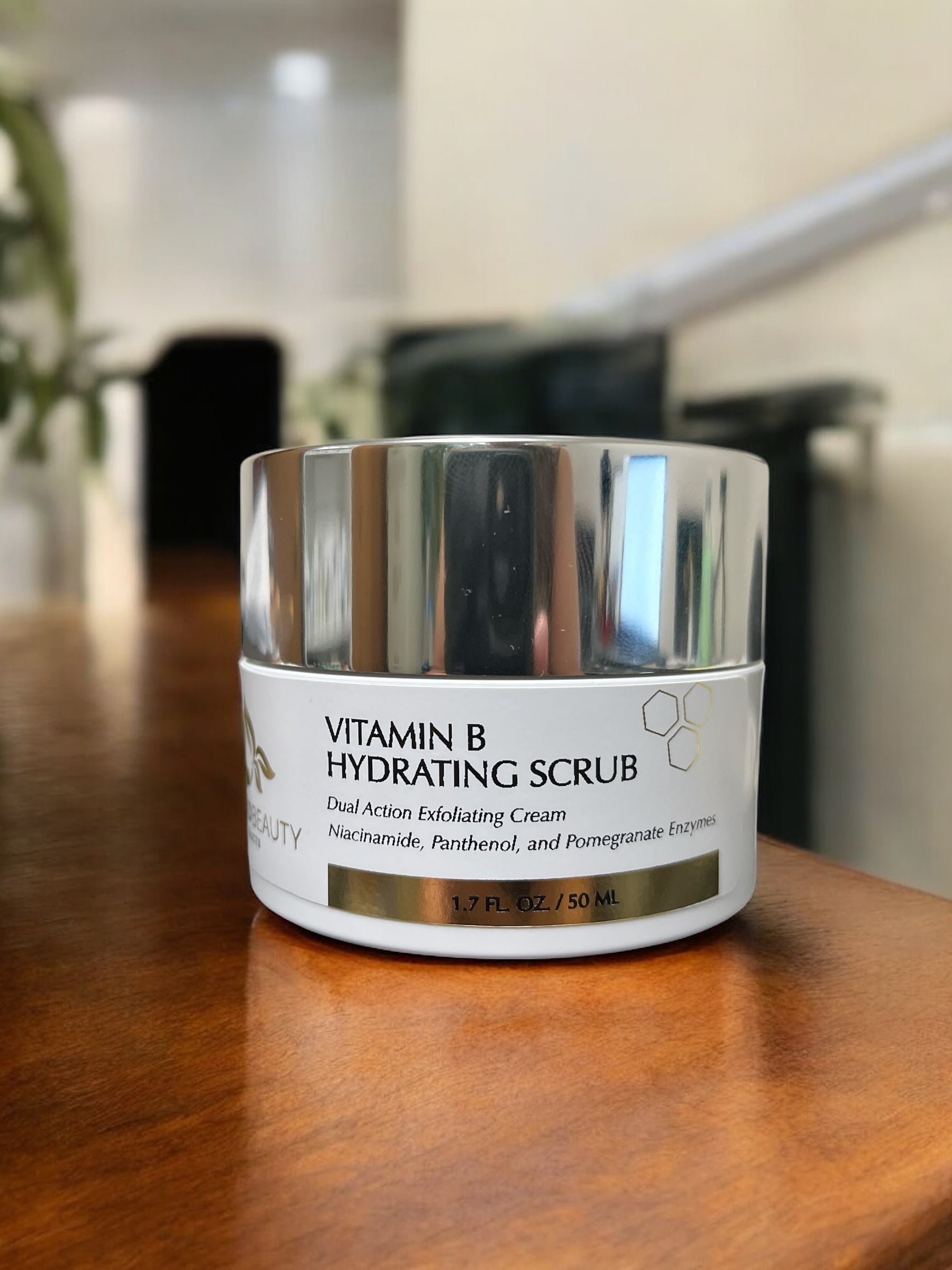 Lifestyle photograph of Reiland Vitamin B Hydrating Scrub placed on a wooden table with blurred indoor background, emphasizing the luxurious silver lid and clean branding.