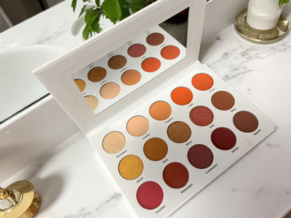Open Velvet Bloom 15-color eyeshadow palette by Reiland Beauty Products with built-in mirror, showcasing matte and shimmer shades on a white marble vanity with gold and green plant accents.