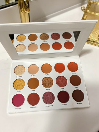 Velvet Bloom 15-color eyeshadow palette by Reiland Beauty Products, open to reveal warm matte and shimmer shades with a built-in mirror, displayed on a white vanity near a gold accessory tray.