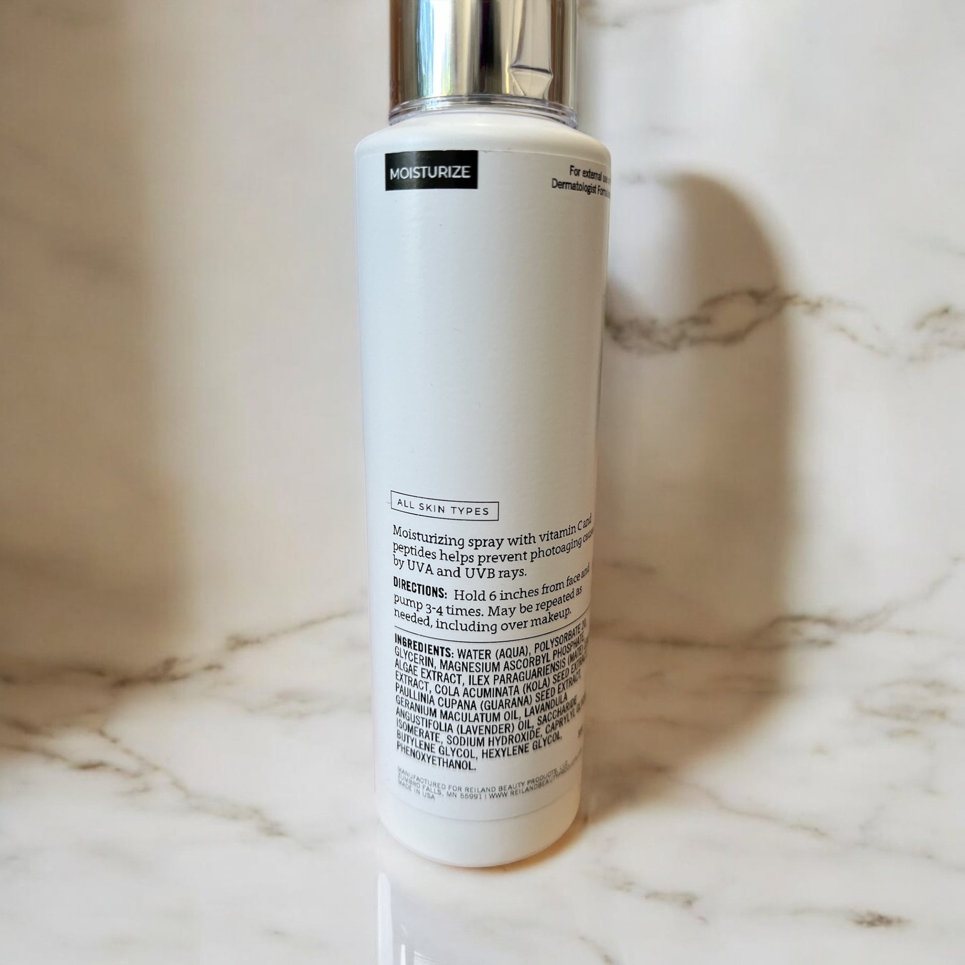 Reiland Vital-C Hydrating Mist – back label showing ingredients, usage directions, and benefits of this Vitamin C-infused moisturizing face mist on a marble surface.